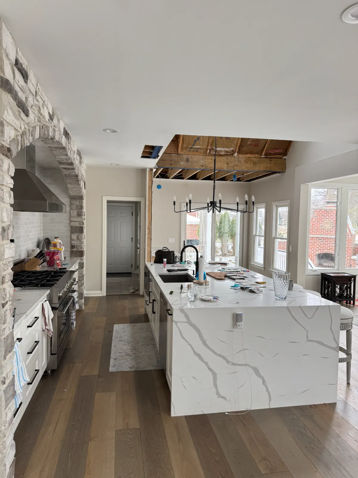 Modern kitchen with marble island, stone arch, and exposed ceiling beams showing renovation work.