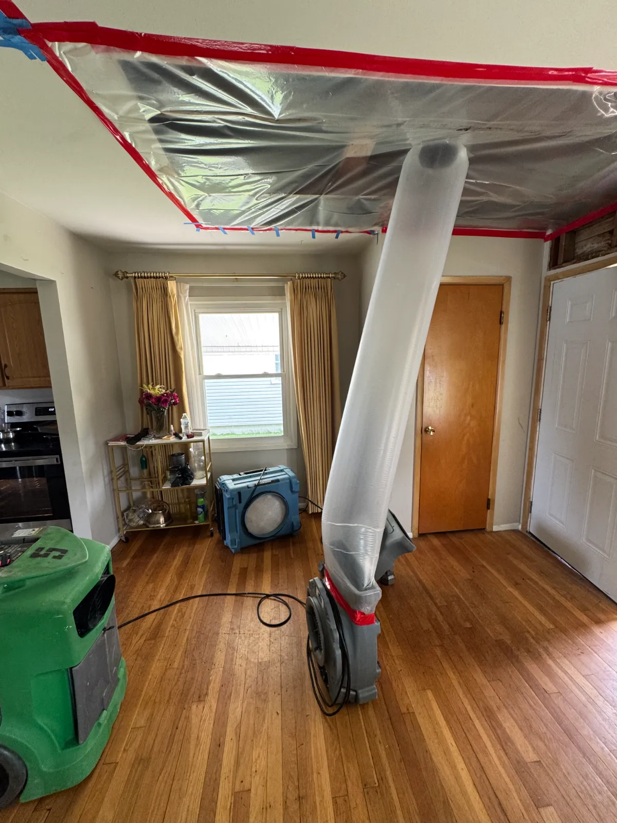 Room with hardwood floor, air scrubbers, and plastic sheet taped to ceiling for flood damage removal.