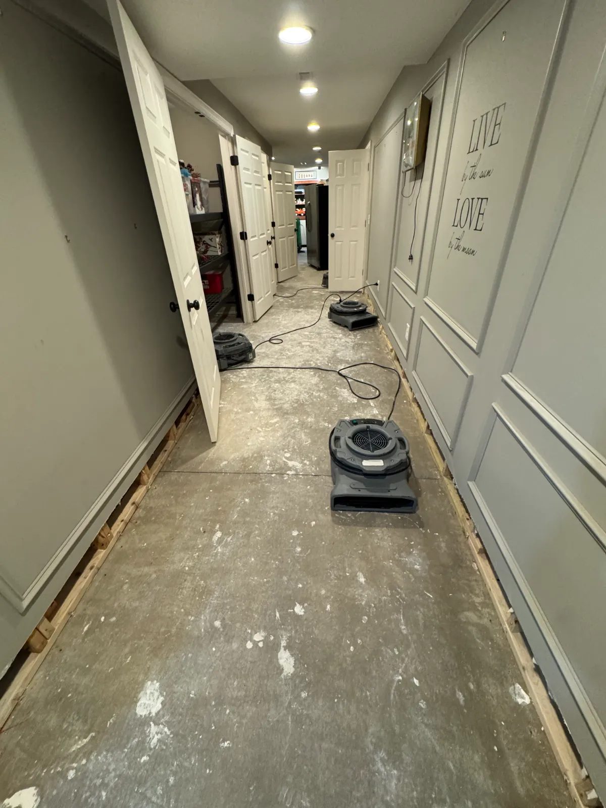 Hallway with baseboards removed and three air movers drying the floor and walls after water damage.