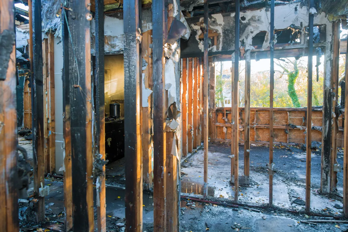 Interior of a house showing severely charred wooden framing and fire damage with debris on the floor.