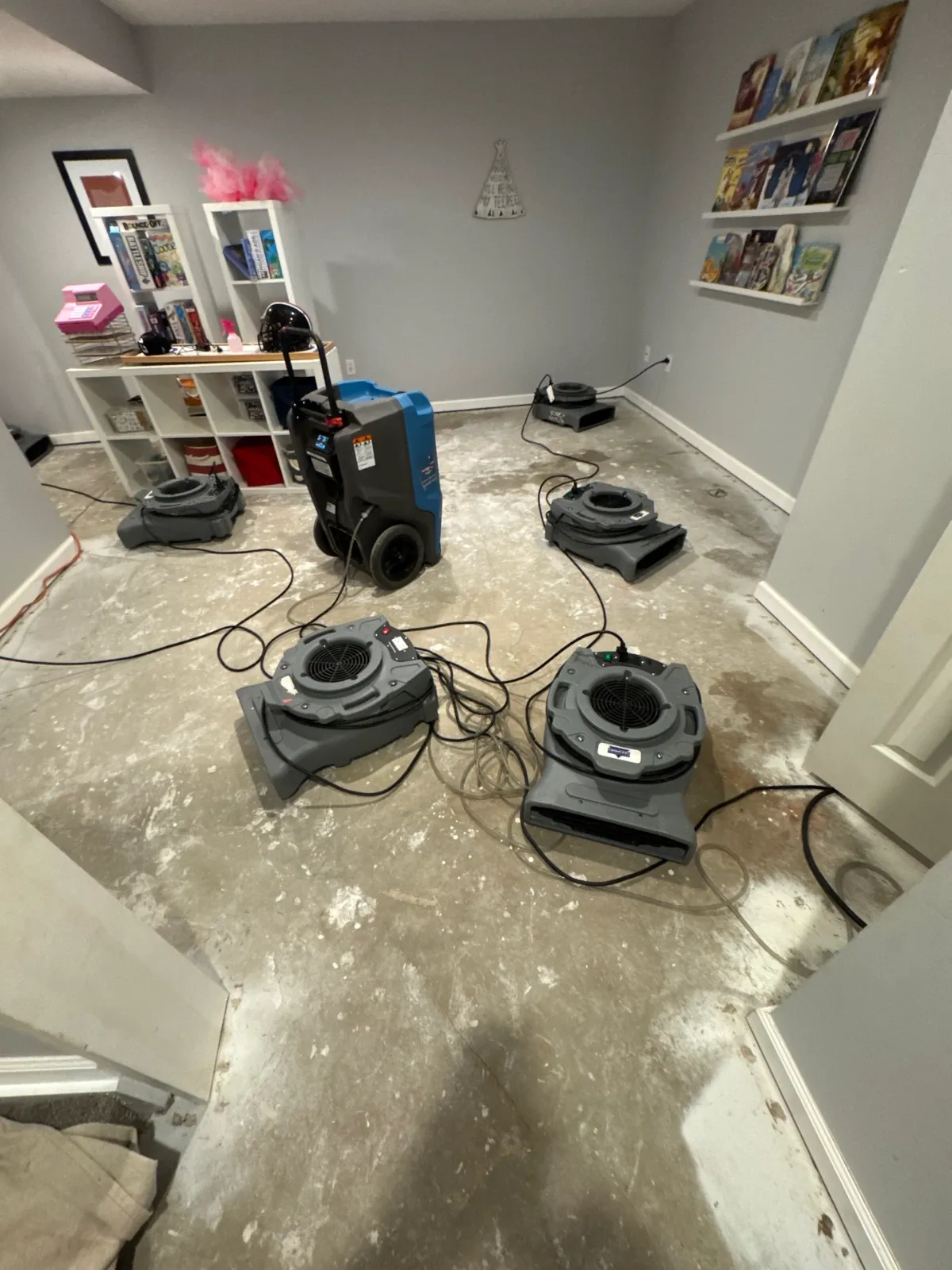 Basement room with water damage drying machines on floor with wet, stained concrete surface.
