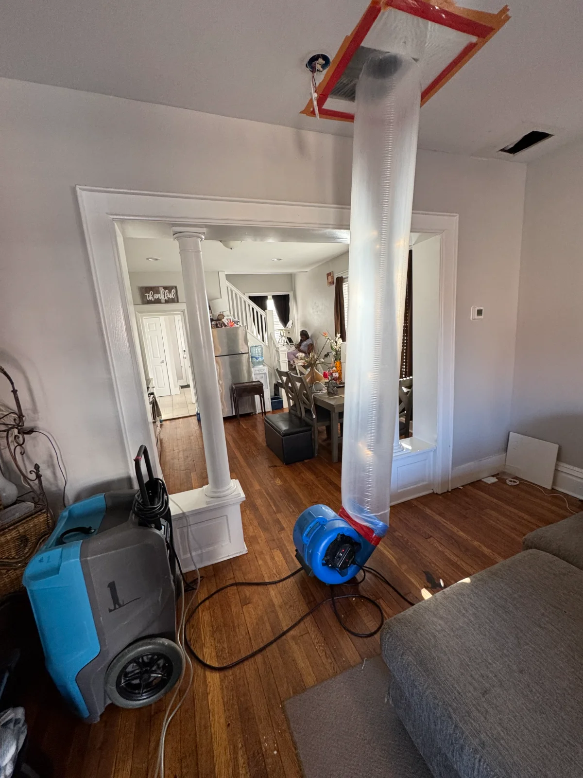 Air blower machine with a long plastic duct attached to a ceiling vent in a living room.