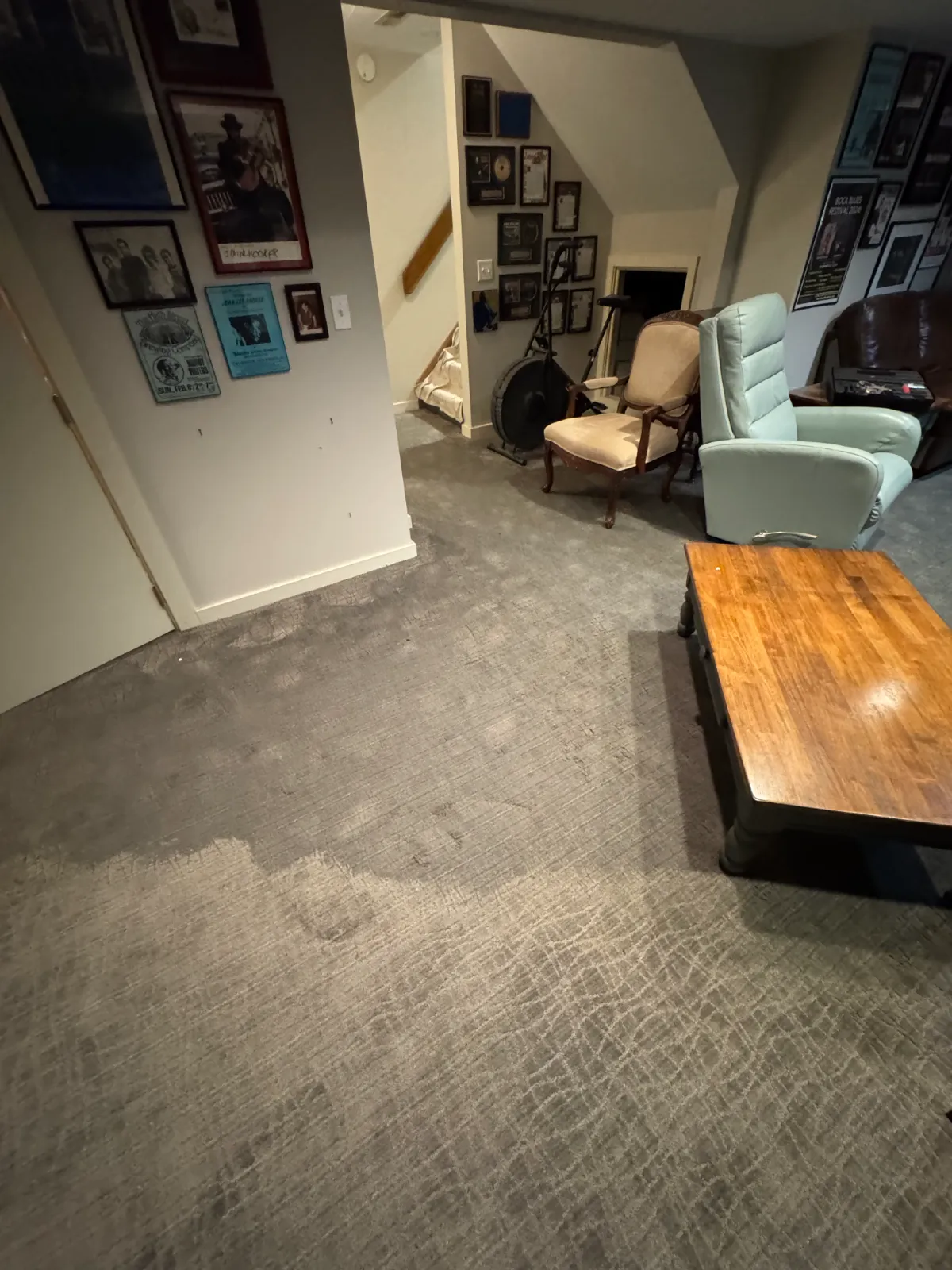 Basement room with wet carpet, several chairs, wood table, and walls decorated with framed photos and plaques.