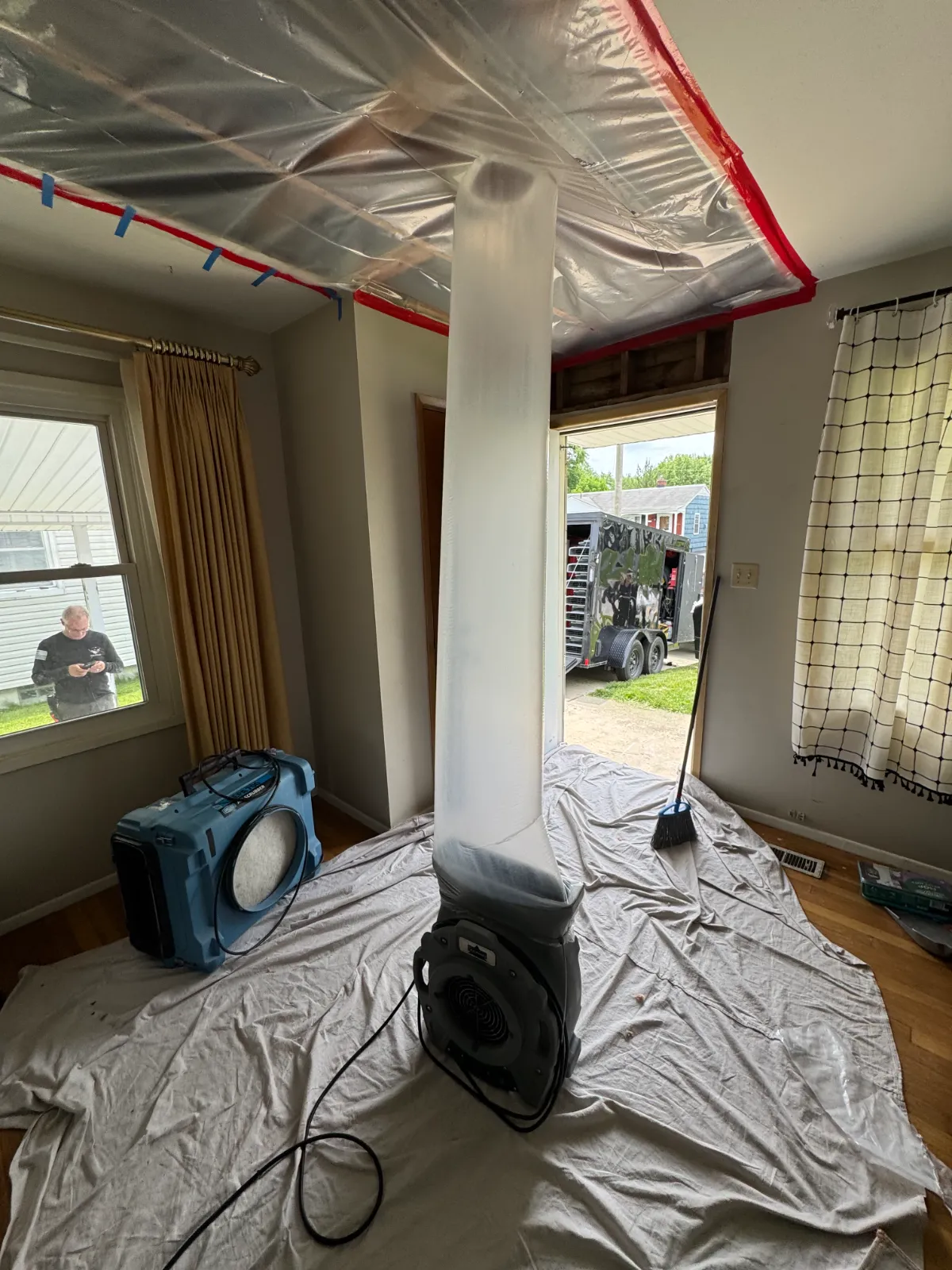 Air blower attached to a plastic sheet on ceiling for drying water damage inside a room.