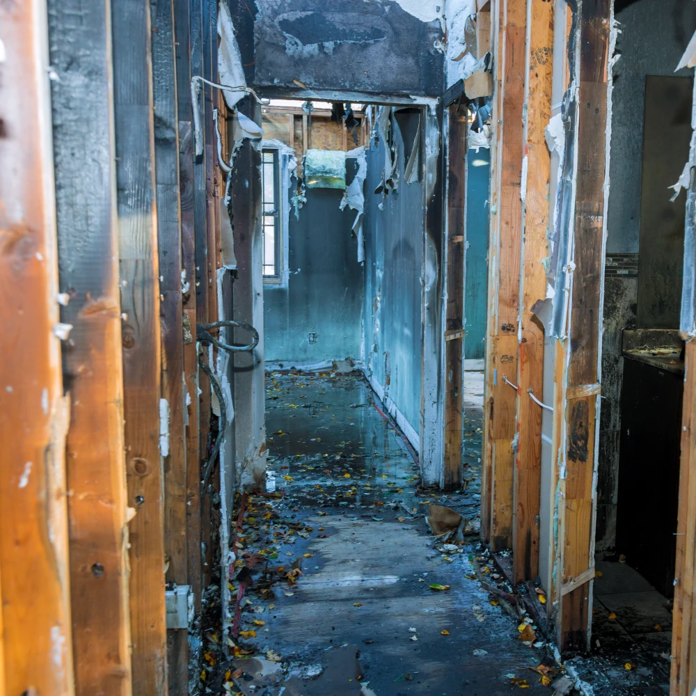 Hallway of a building severely damaged by fire with charred walls and debris on the wet floor.