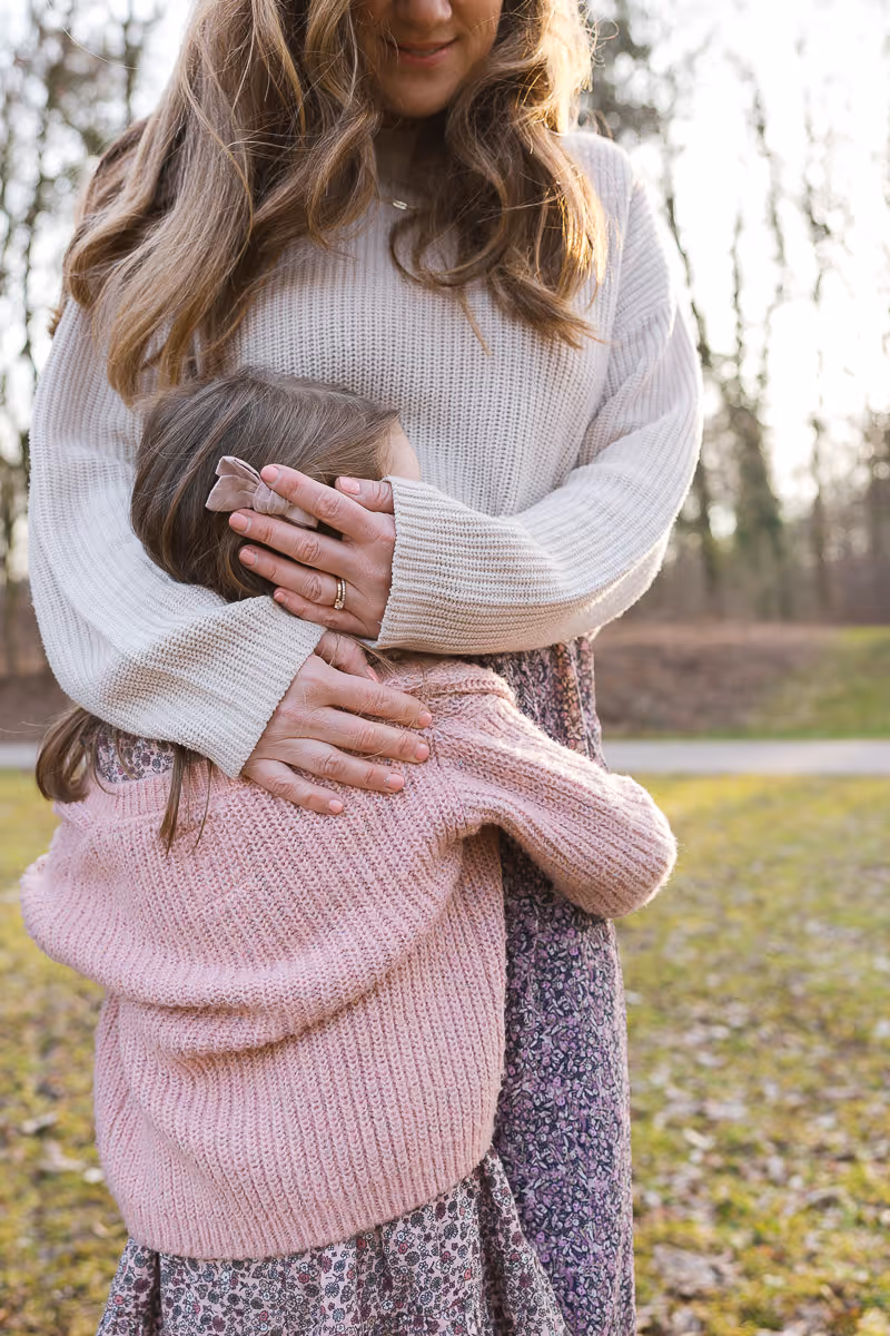 Mother wraps her arms around her daughters head into her tummy.