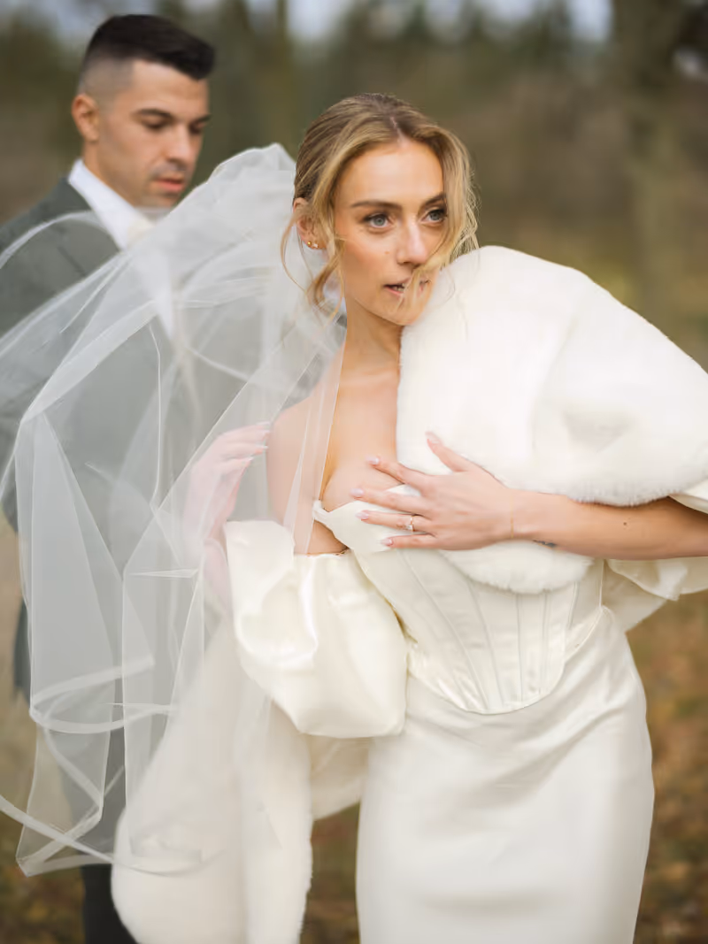 Bride fixes her wedding dress with groom behind her. 