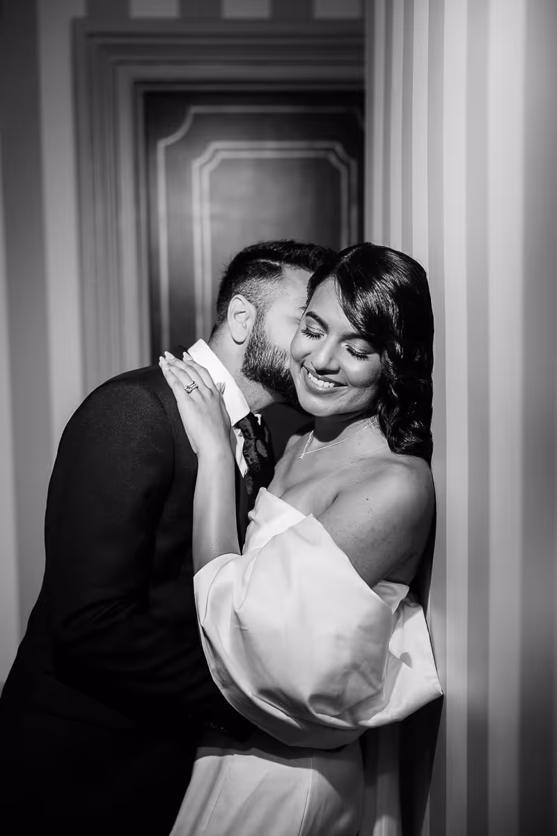Groom kissing his bride inside hotel hallway with flash.