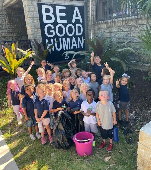 A group of TVM students stand in front of a sign reading, "Be a good human".