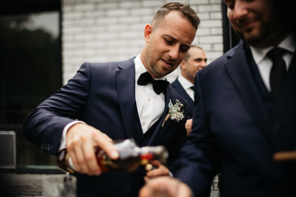 groom pouring whiskey on pec waterfront deck
