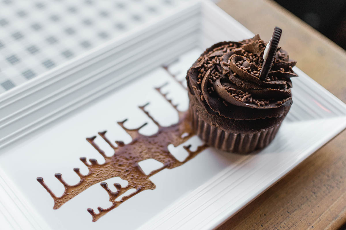 A chocolate cupcake delicately placed on a rectangular plate, with chocolate sauce spread across the plate.