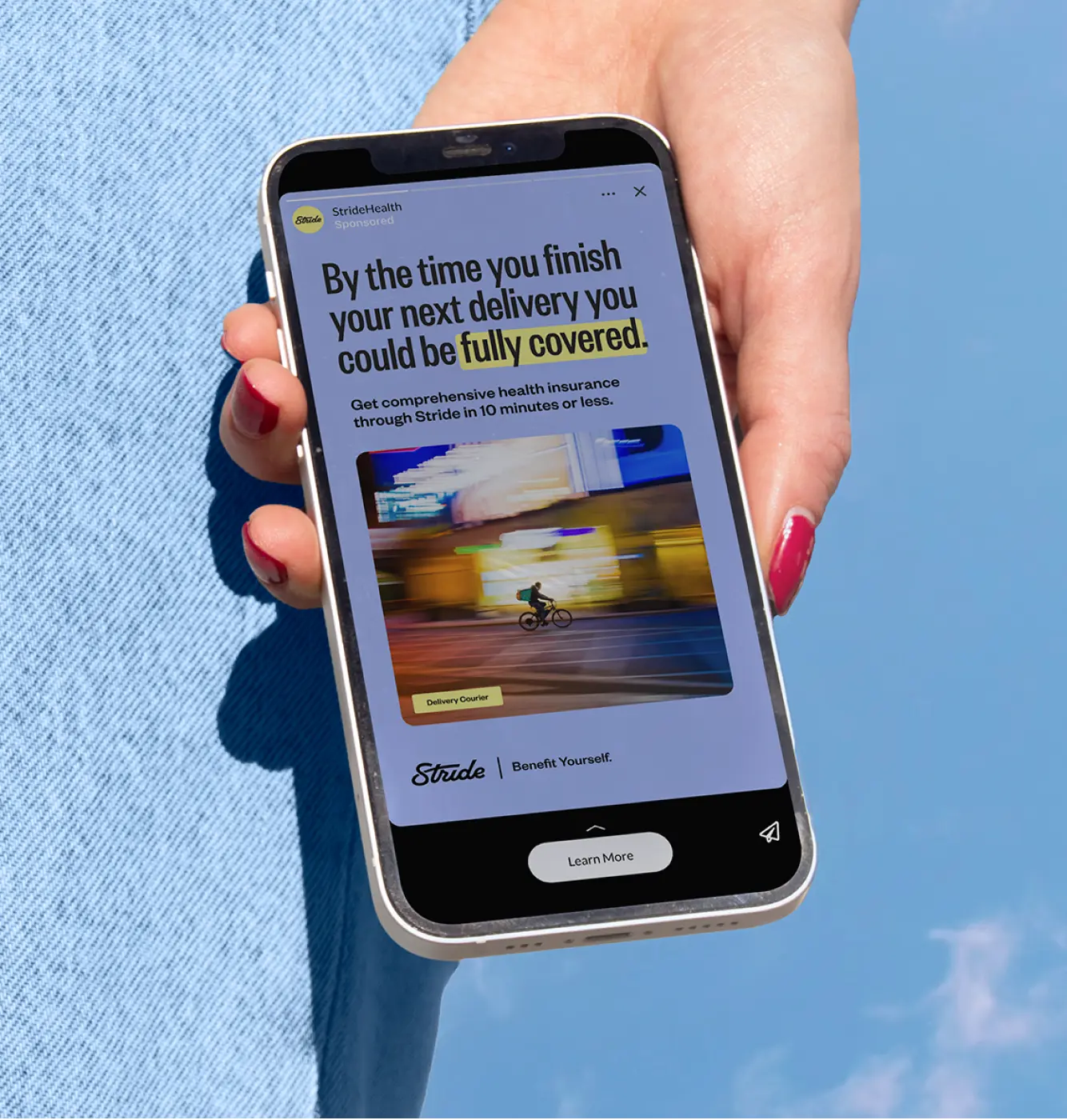 Hand holding phone showing StrideHealth ad about getting health insurance fully covered for delivery workers.
