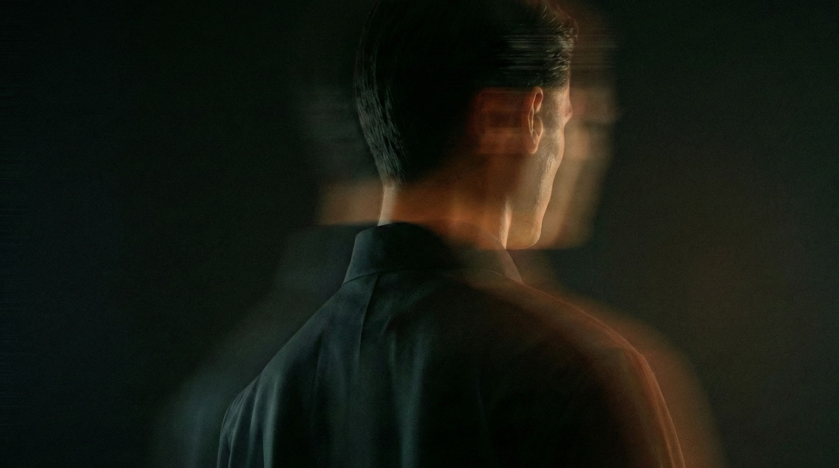 Blurred, double-exposed profile of a man in a dark shirt against a dark background.