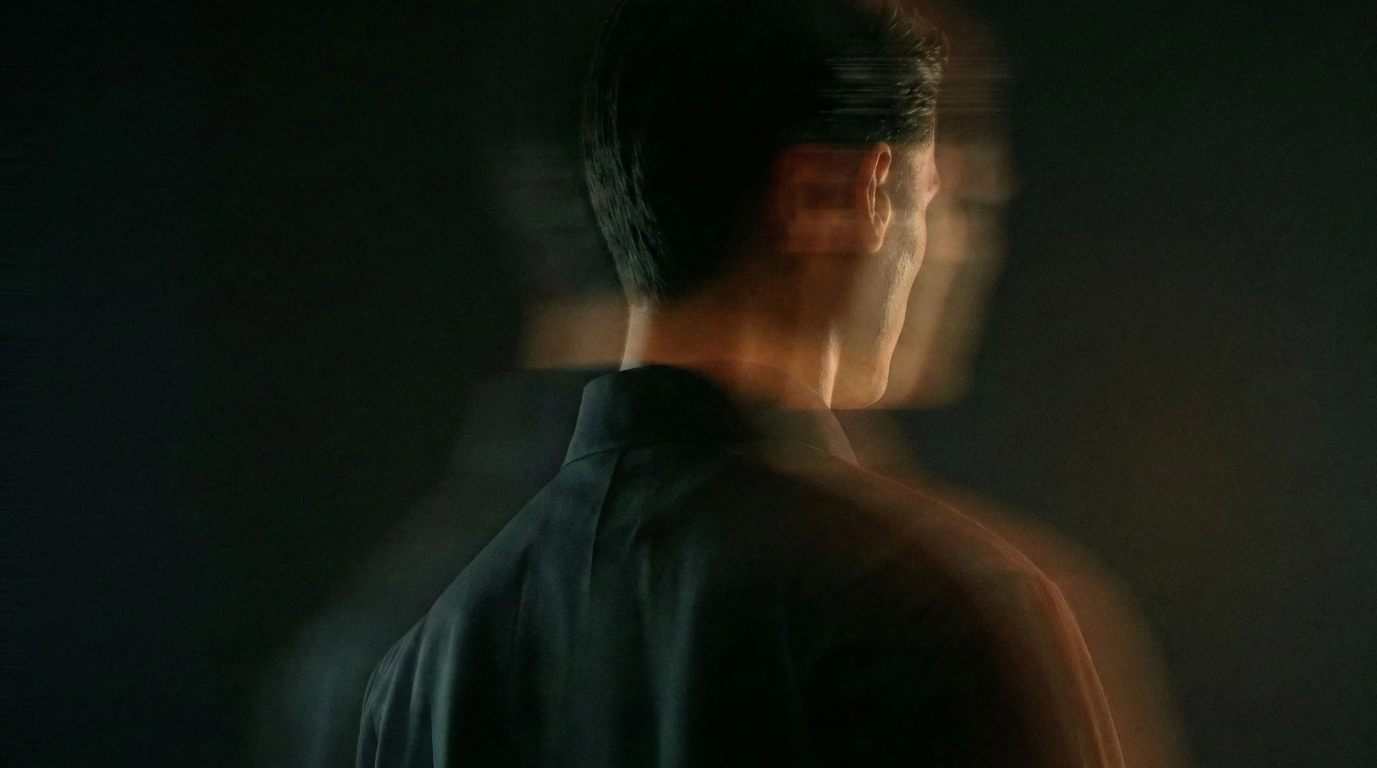 Blurred, double-exposed profile of a man in a dark shirt against a dark background.