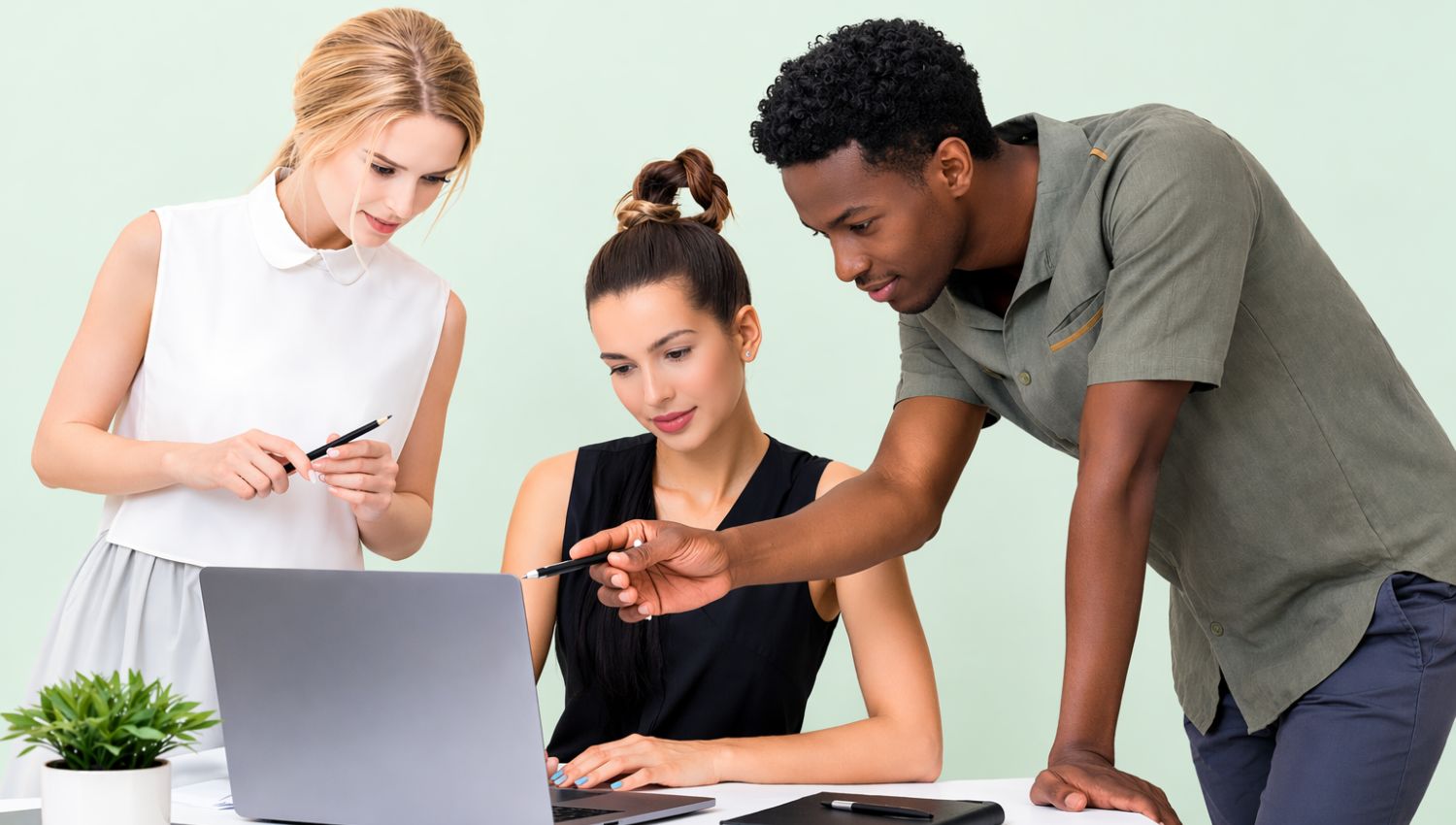 Three professionals collaborating at a desk, reviewing work together on a laptop in a modern office setting.