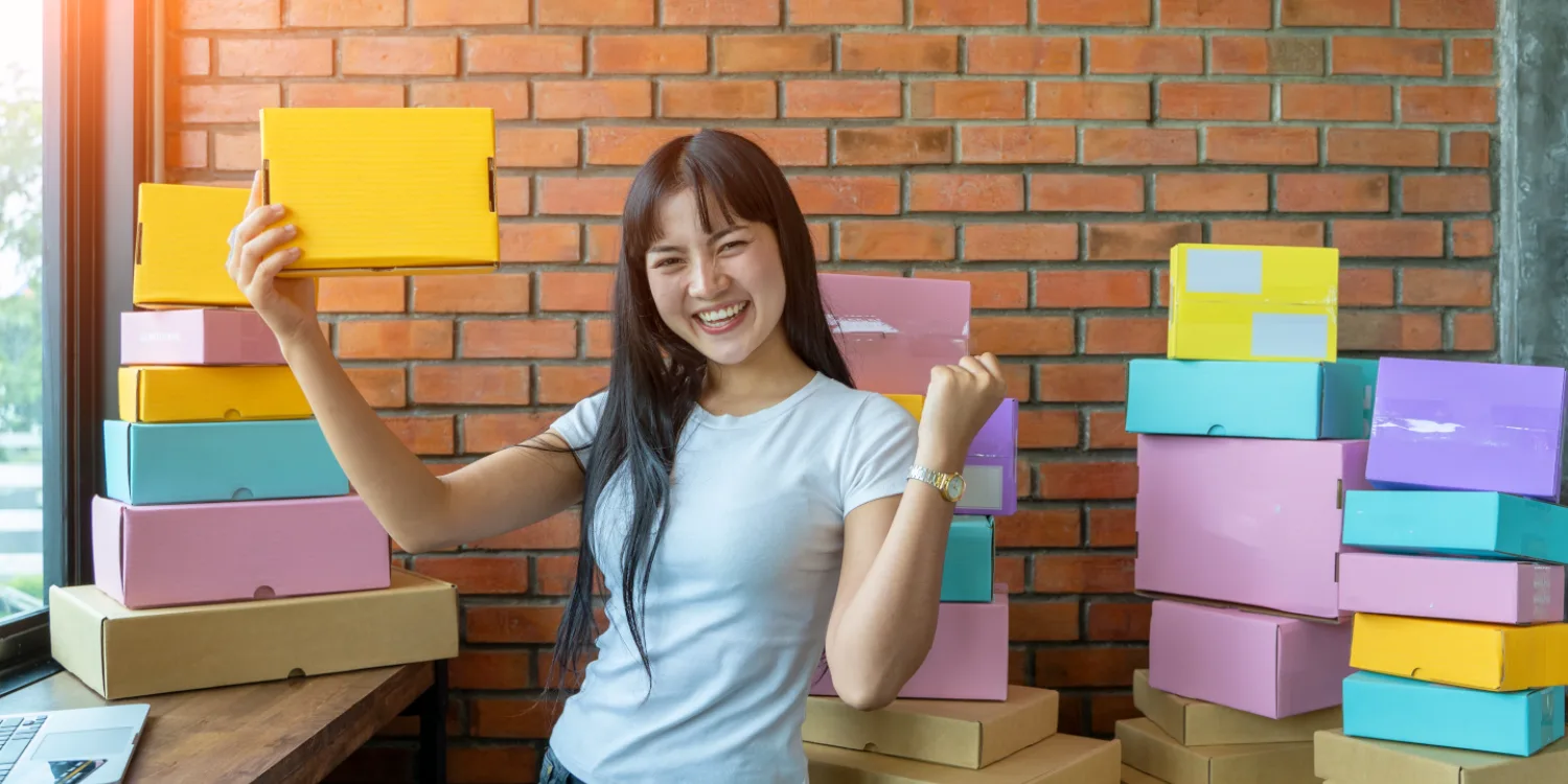 Smiling online seller surrounded by colourful parcels for Awin vs TAG affiliate network comparison article.