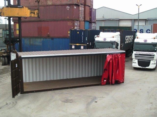 A brown 40ft side curtain shipping container with full-length side opening curtain in bright red for storage and distribution. The container doors are open. It is situated in a container depot with other containers.