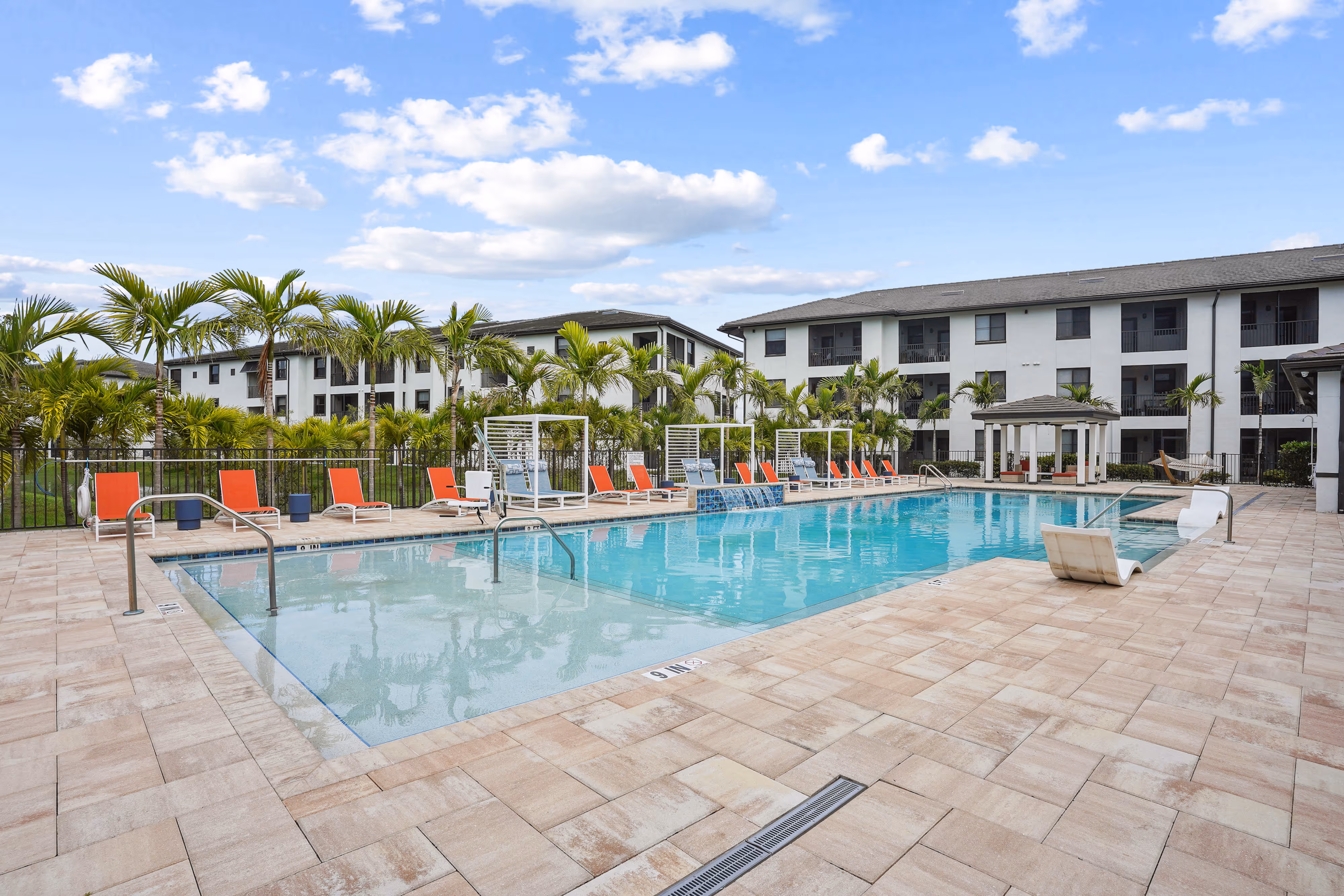 Spacious community swimming pool surrounded by orange lounge seating and palm trees, showcasing a tropical retreat at The Edge at Fort Myers, FL.