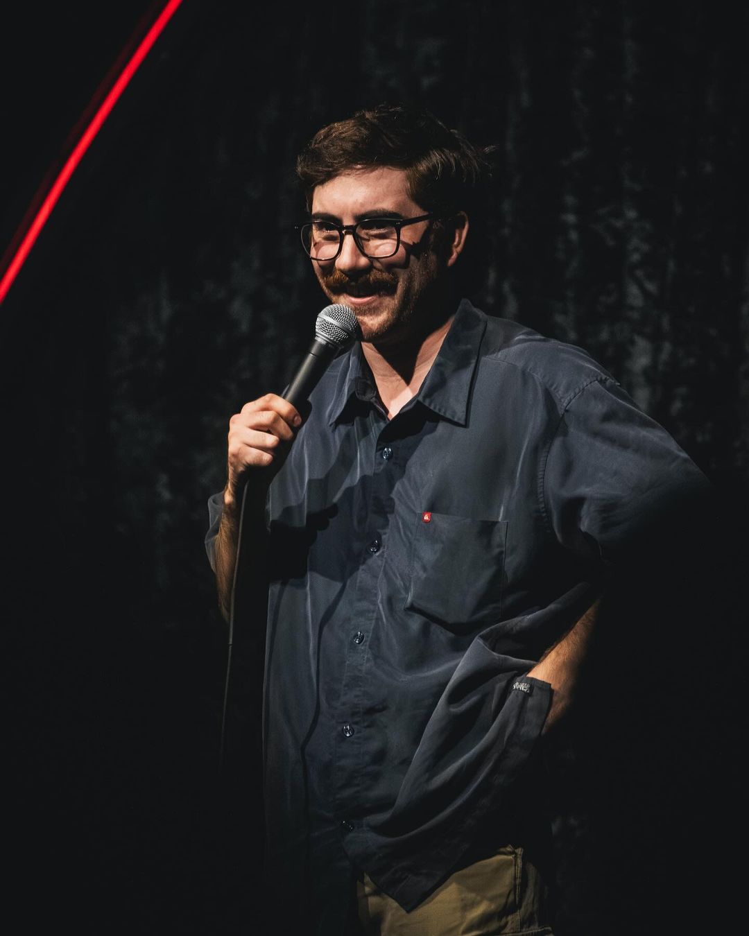 A man holding a microphone in front of a dark background.