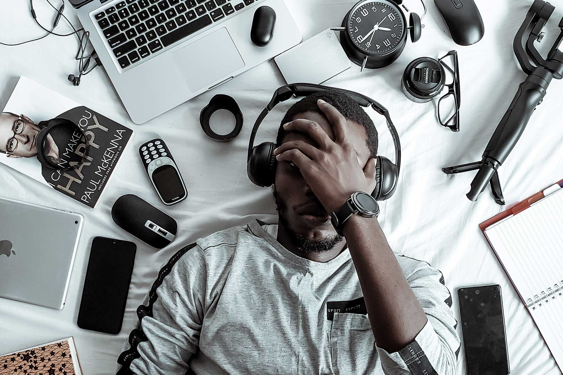 A person listening to podcast with headphones and electronic gadgets surrounding