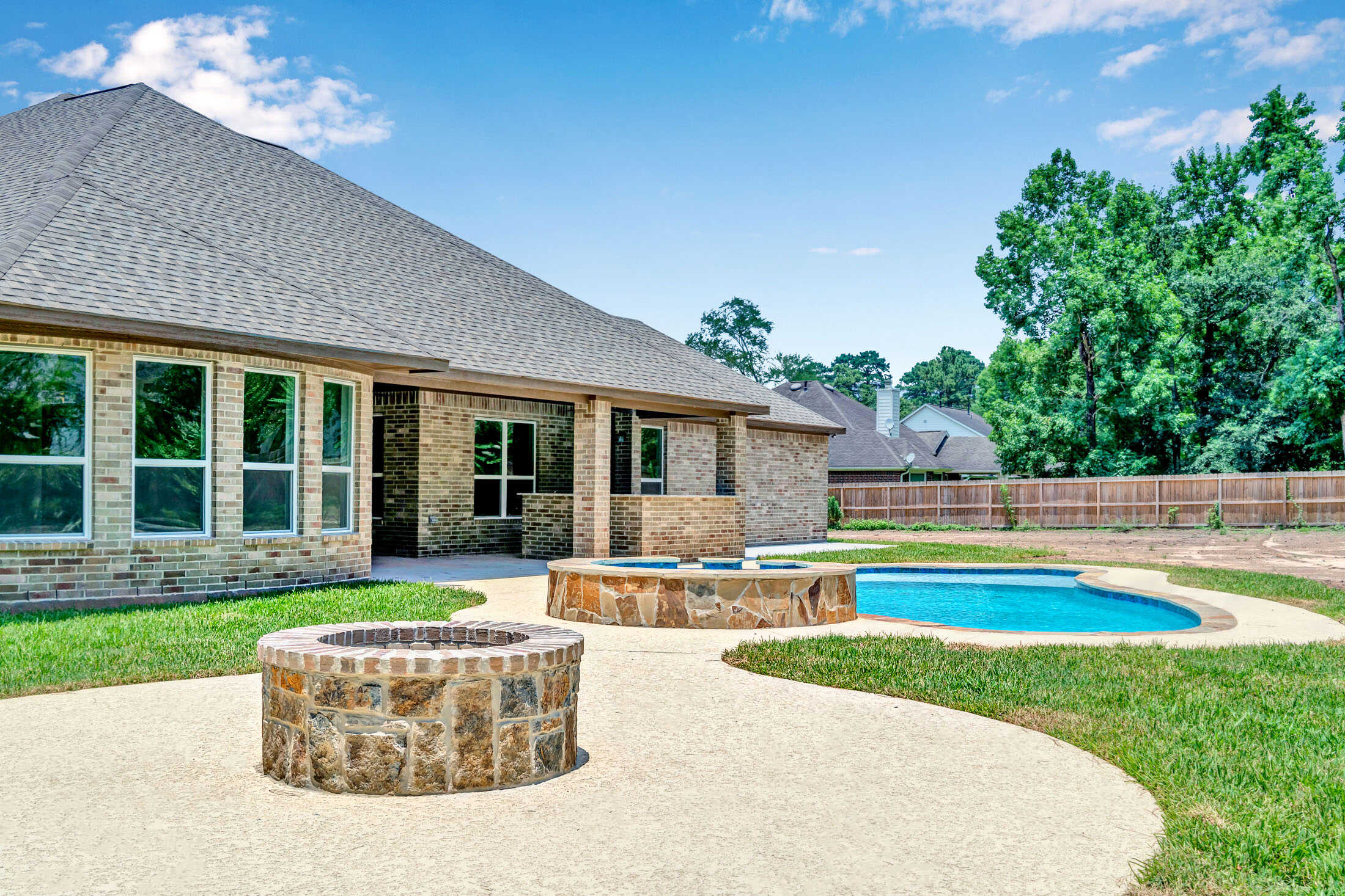 Backyard view of a brick home with a pool, spa, and lawn