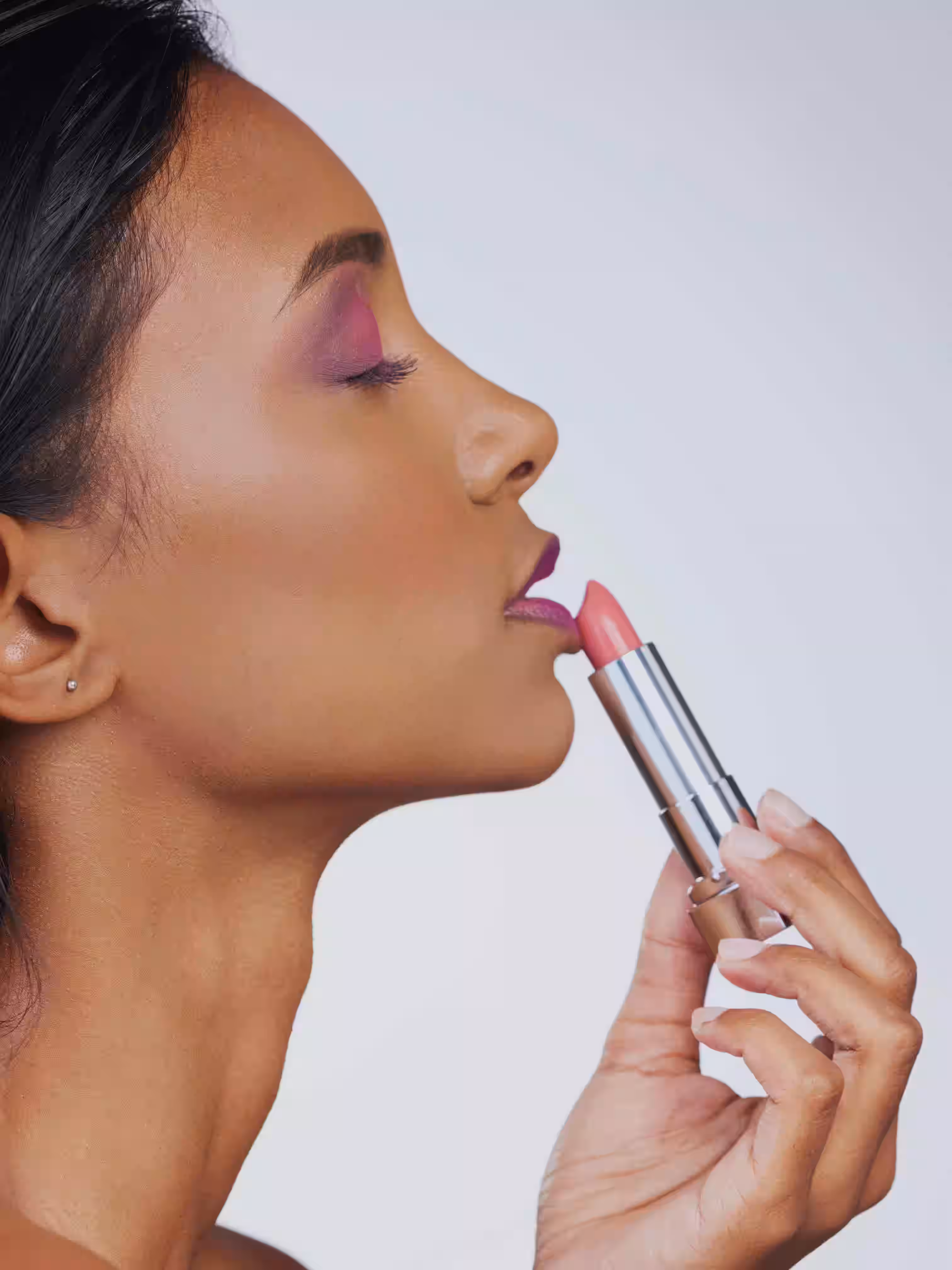 La mujer con una llamativa sombra de ojos morada aplica lápiz labial en un tono rosa claro.