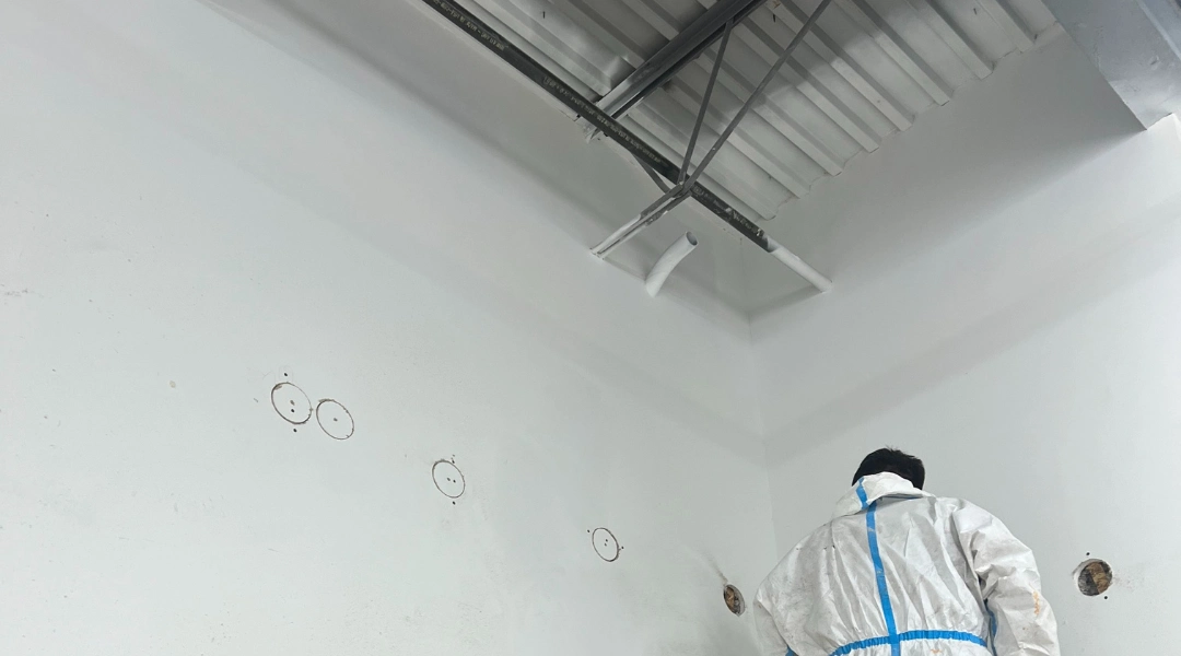 Commercial cellulose insulation installer working on a tall interior wall in a high-ceiling commercial space