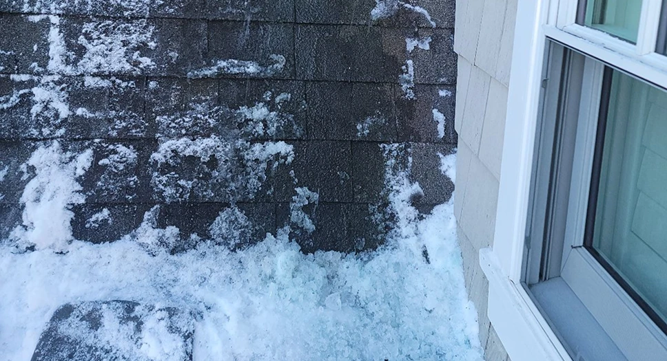 Ice dam salt treatment on a snow-covered shingle roof near a window