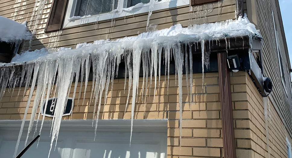 Large icicles hanging from a roof edge, showing ice dam buildup that can be prevented with proper insulation and ventilation