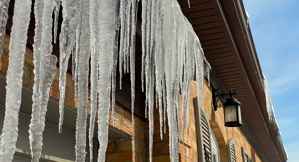 Large icicles hanging from a roof eave, showing ice buildup that can lead to ice dams and winter roof damage