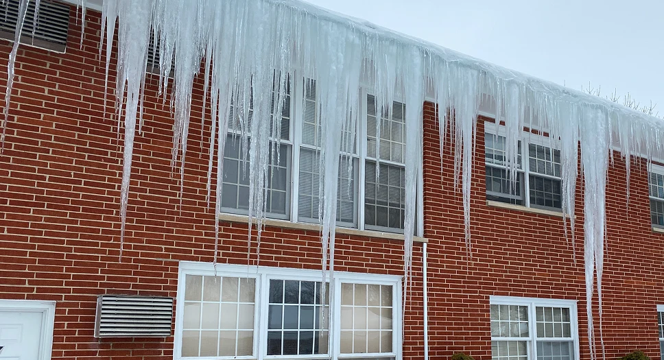 Long icicles hanging from a roof eave, showing ice dam buildup caused by melting snow refreezing at the roof edge