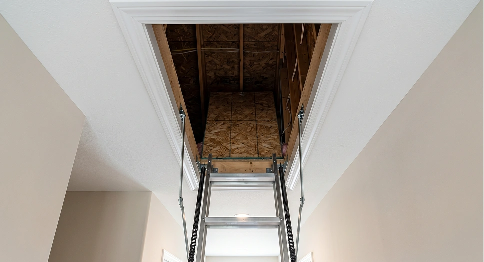 Open attic access door with pull-down ladder viewed from inside a home hallway.