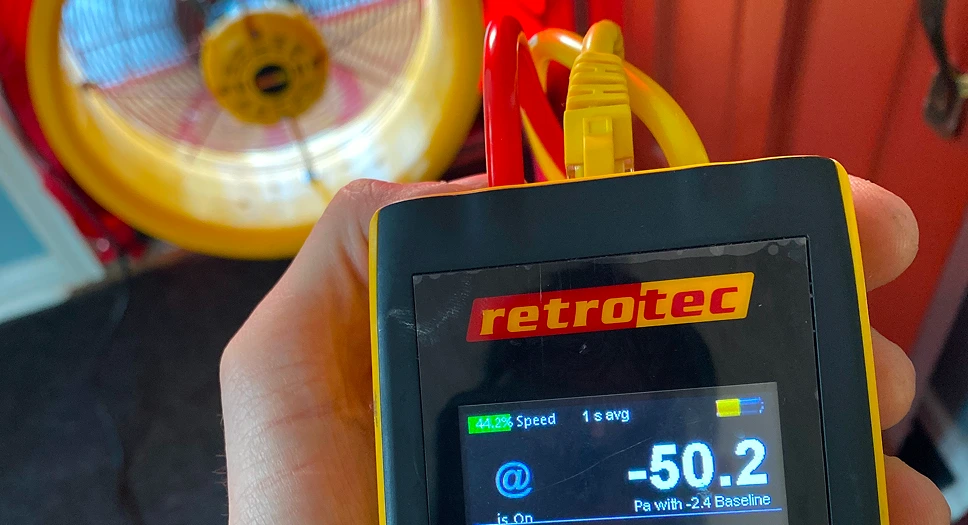 Blower door test equipment showing a digital pressure gauge, diagnostic fan, and airflow tubing used during a home energy audit.