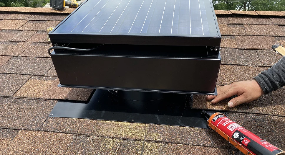 Close-up of a solar attic fan installation with roof flashing and sealant.