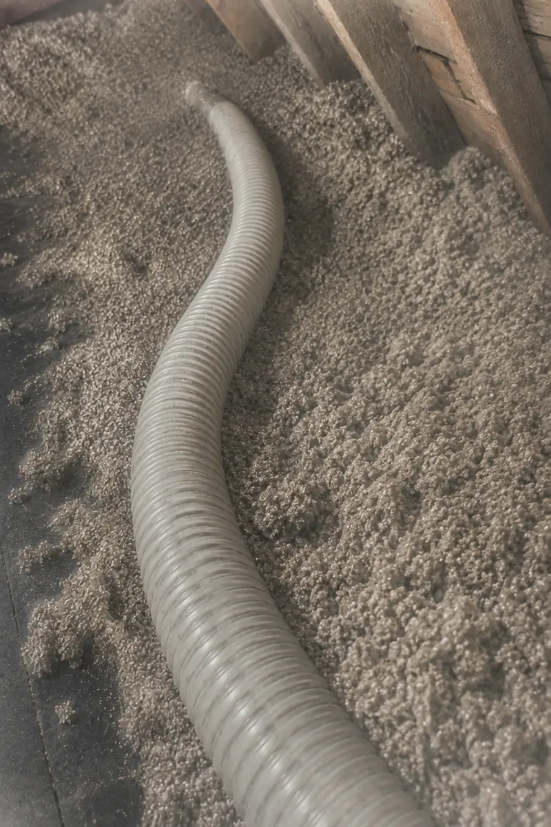 A vacuum hose pulls loose vermiculite from the attic during removal