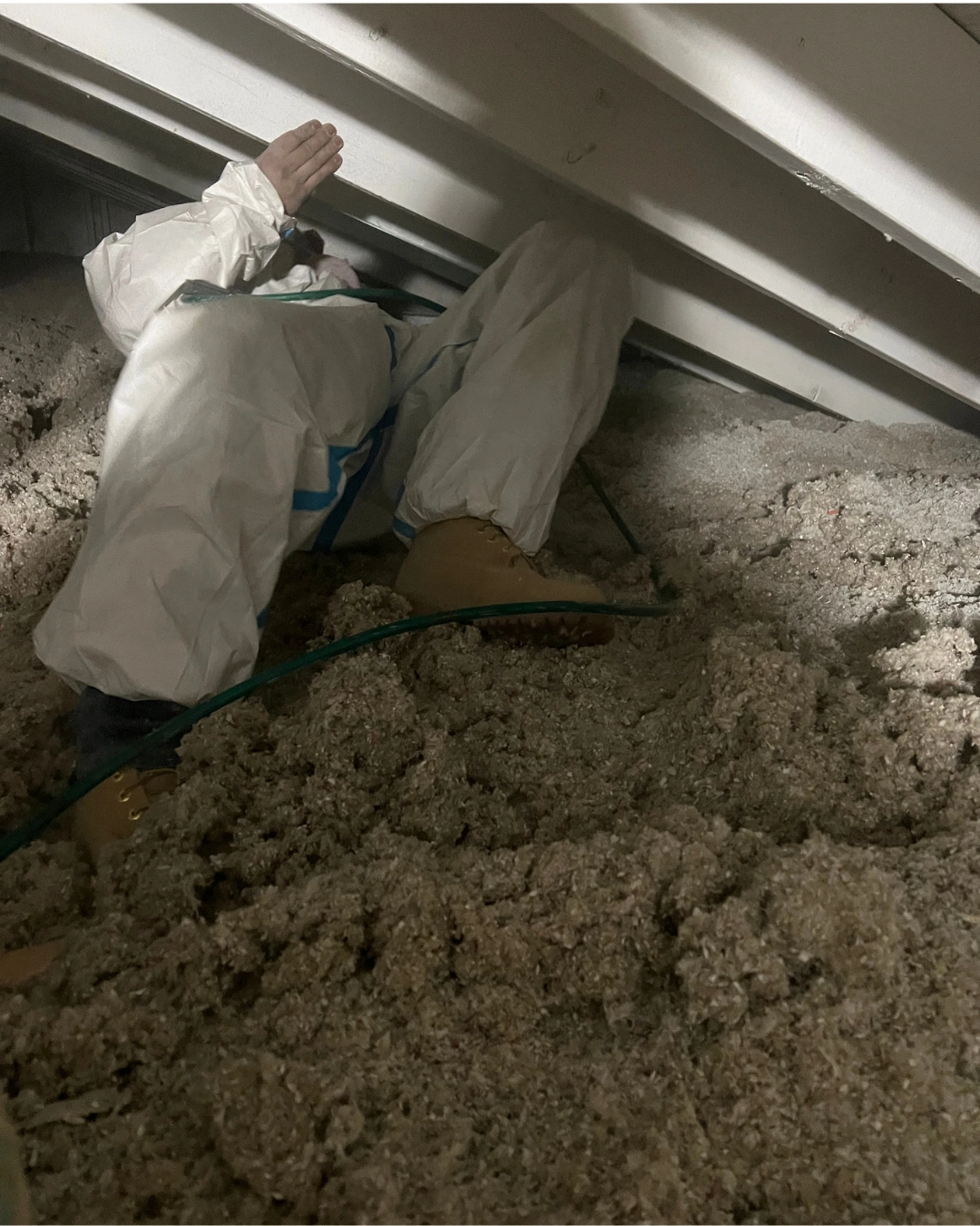 Technician in a protective suit working in a low-clearance attic space filled with deep cellulose loose-fill insulation