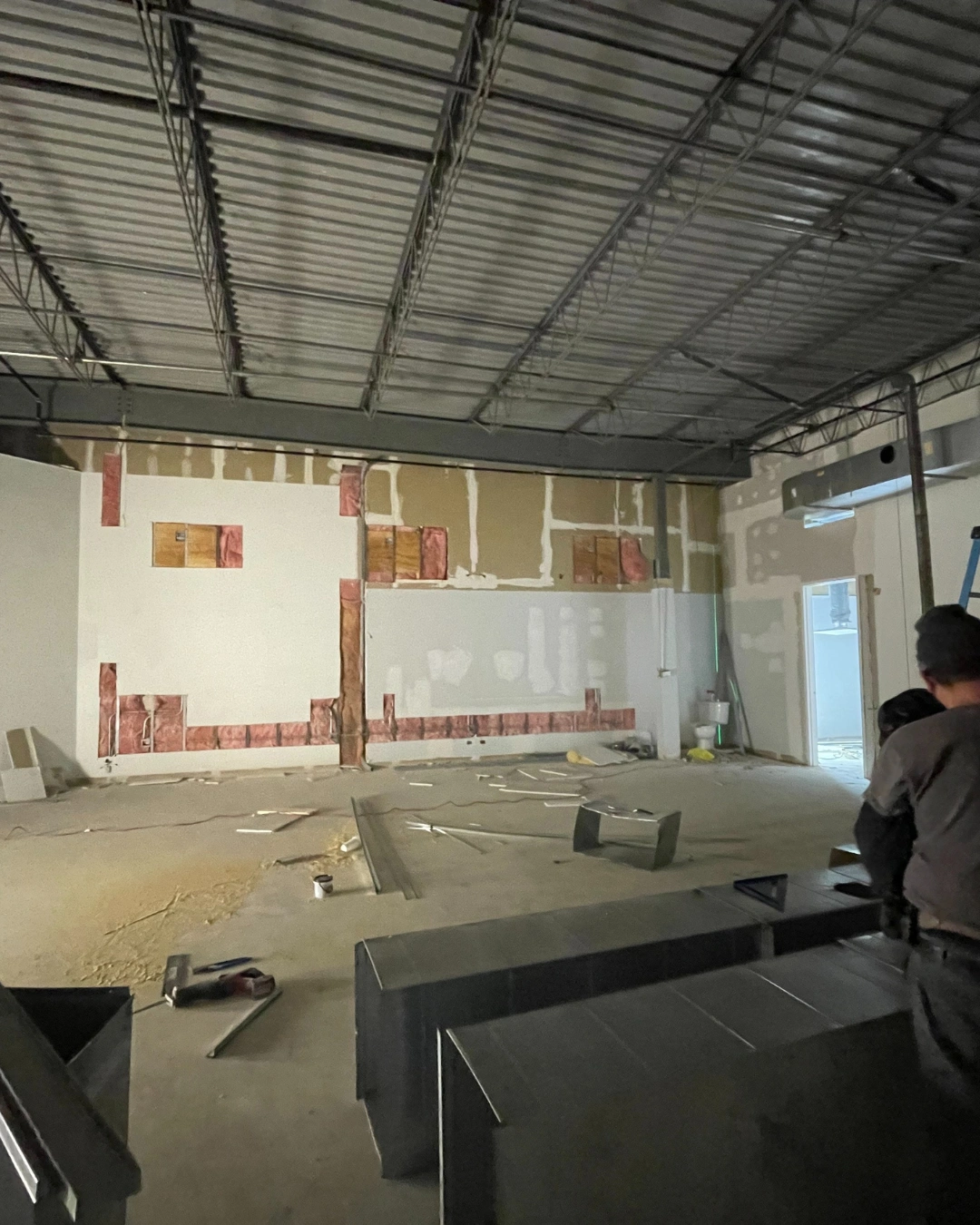 Commercial interior with drywall removed, showing fiberglass insulation present in some wall cavities and missing in others beneath an open steel joist ceiling