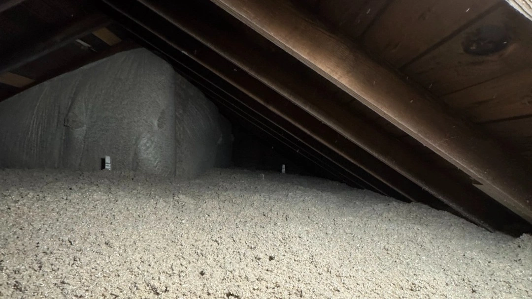 Deep blown-in cellulose insulation covering an attic floor and banked up toward the low eaves under bare wooden rafters
