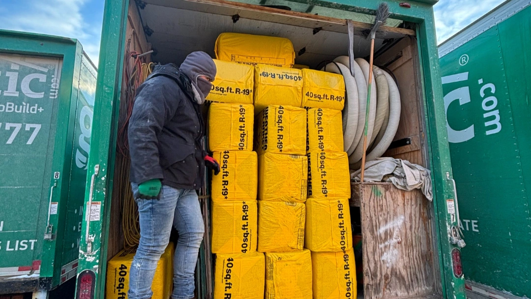 Green Attic worker loading bags of R-19 fiberglass batt insulation into the back of a company truck on a cold morning