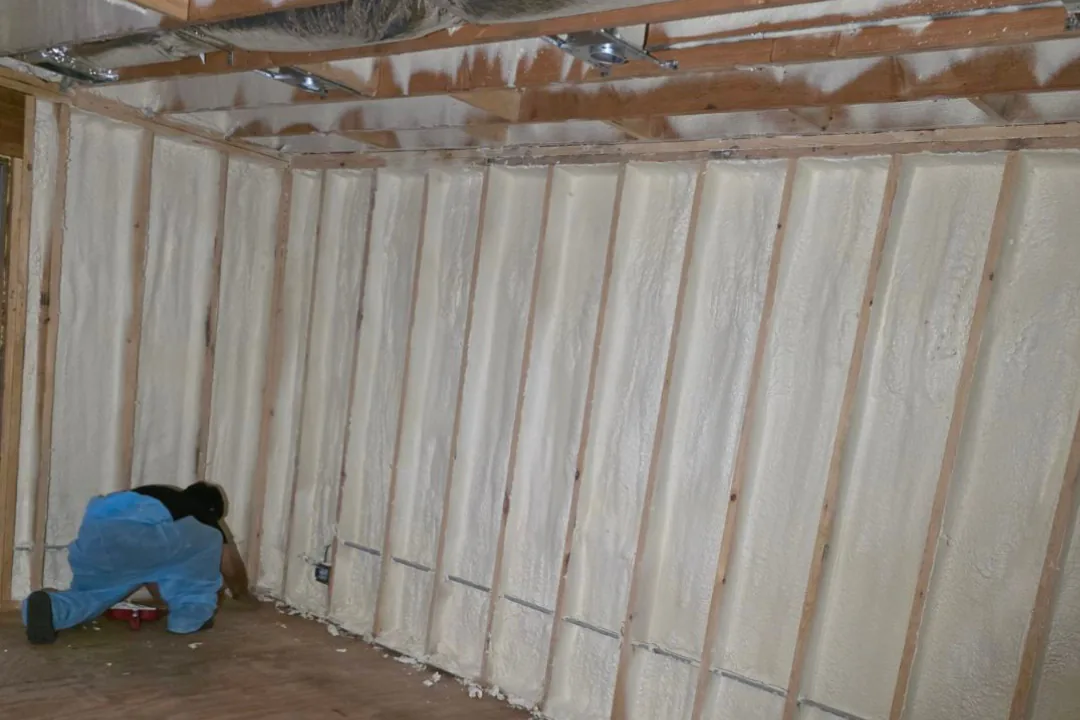 Installer applying spray foam insulation to wall cavities and ceiling joists during a home insulation project