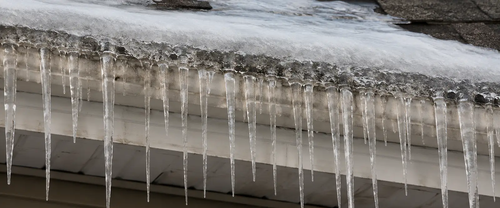 Ice dam with long icicles hanging from a snow-covered roof edge and gutter