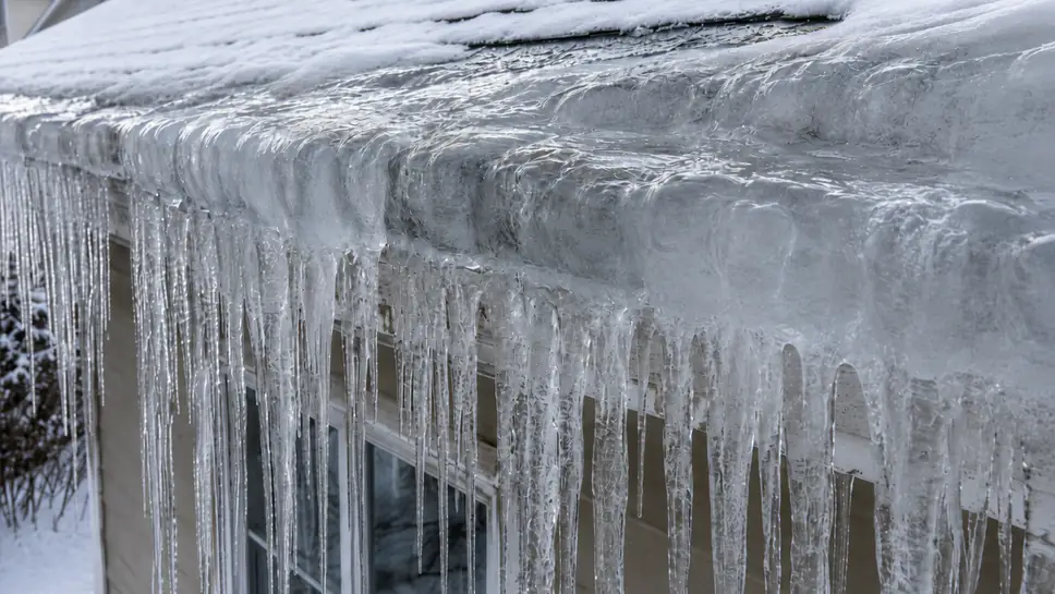 Thick ice dam frozen across a gutter with icicles hanging from the roof edge