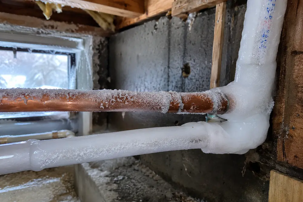 Copper and PEX water pipes covered in ice inside an uninsulated basement