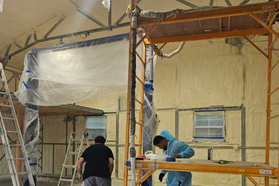 Green Attic crew spraying foam insulation inside a pole barn with masking over the openings