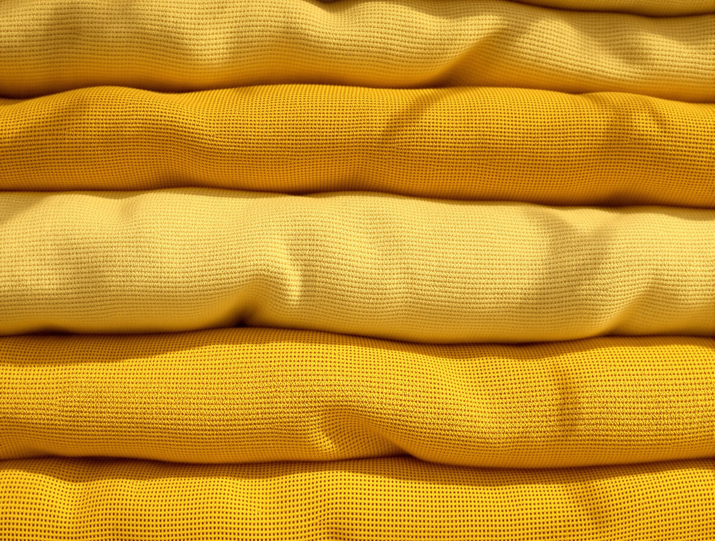 Textures de linge coton plié en tons chauds, jaune moutarde et crème, lumière naturelle chaude
