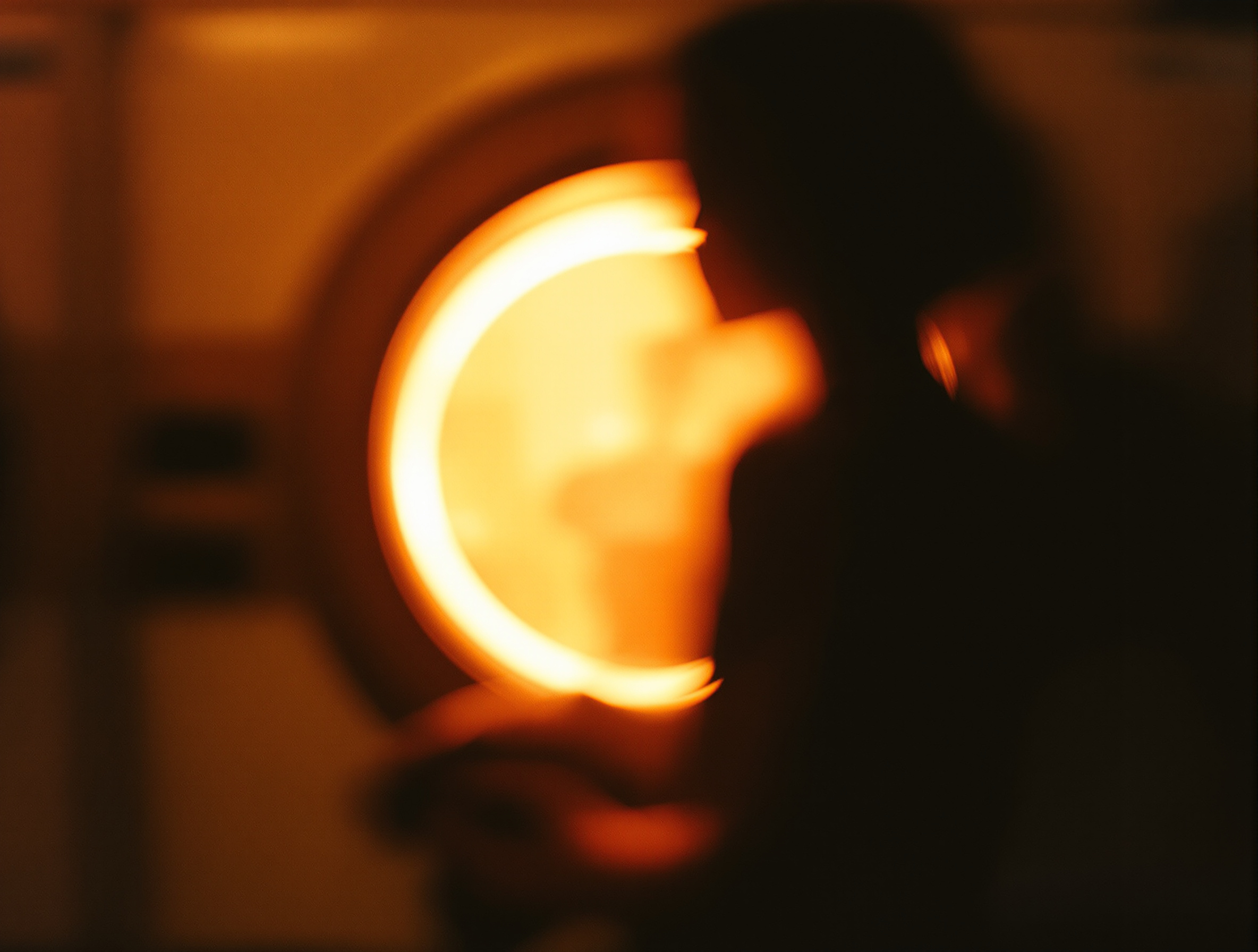 Silhouette de dos floue devant un lave-linge, hublot lumineux chaud, ambiance laverie années 70