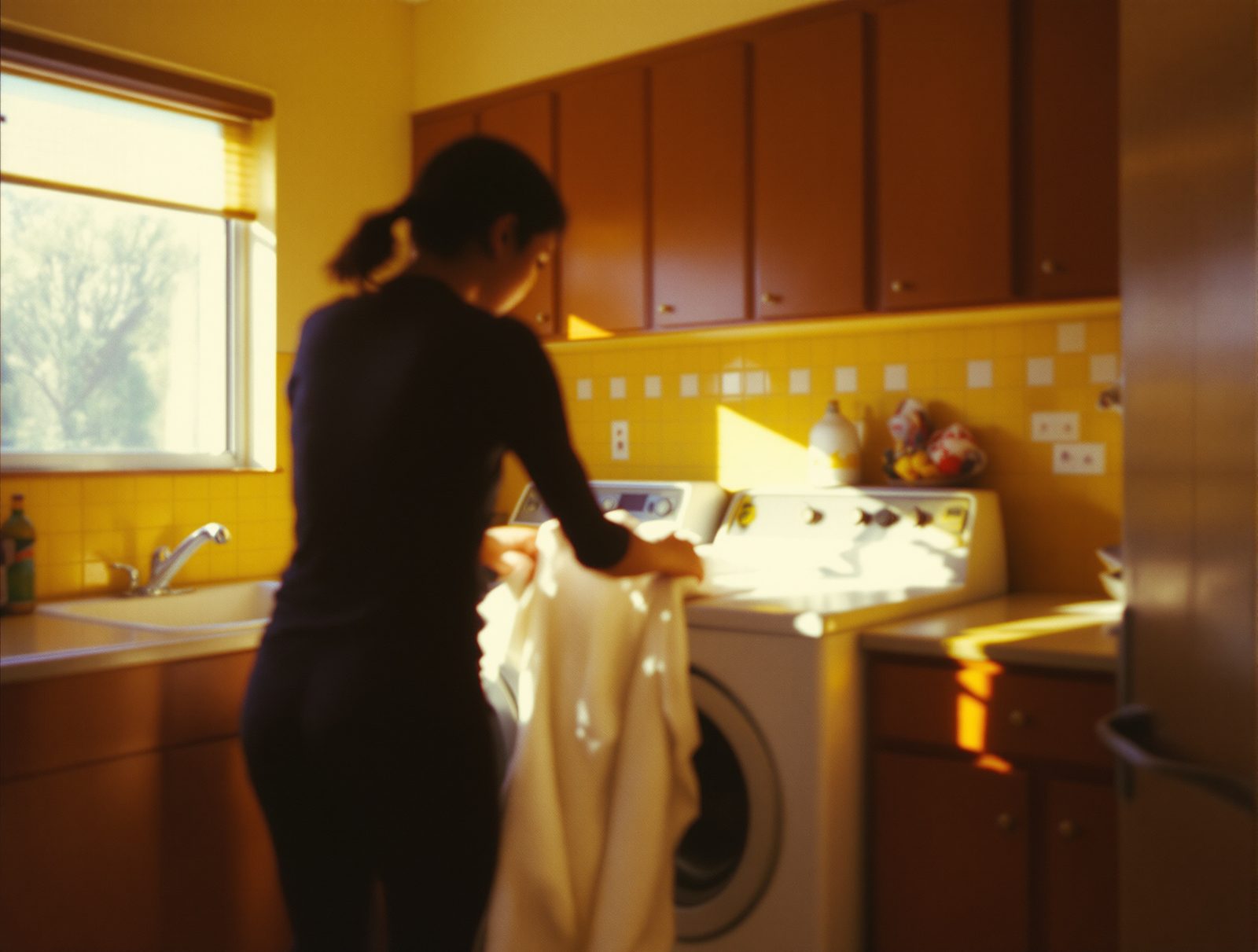 Silhouette floue de dos chargeant du linge dans un sèche-linge, ambiance lumineuse années 70
