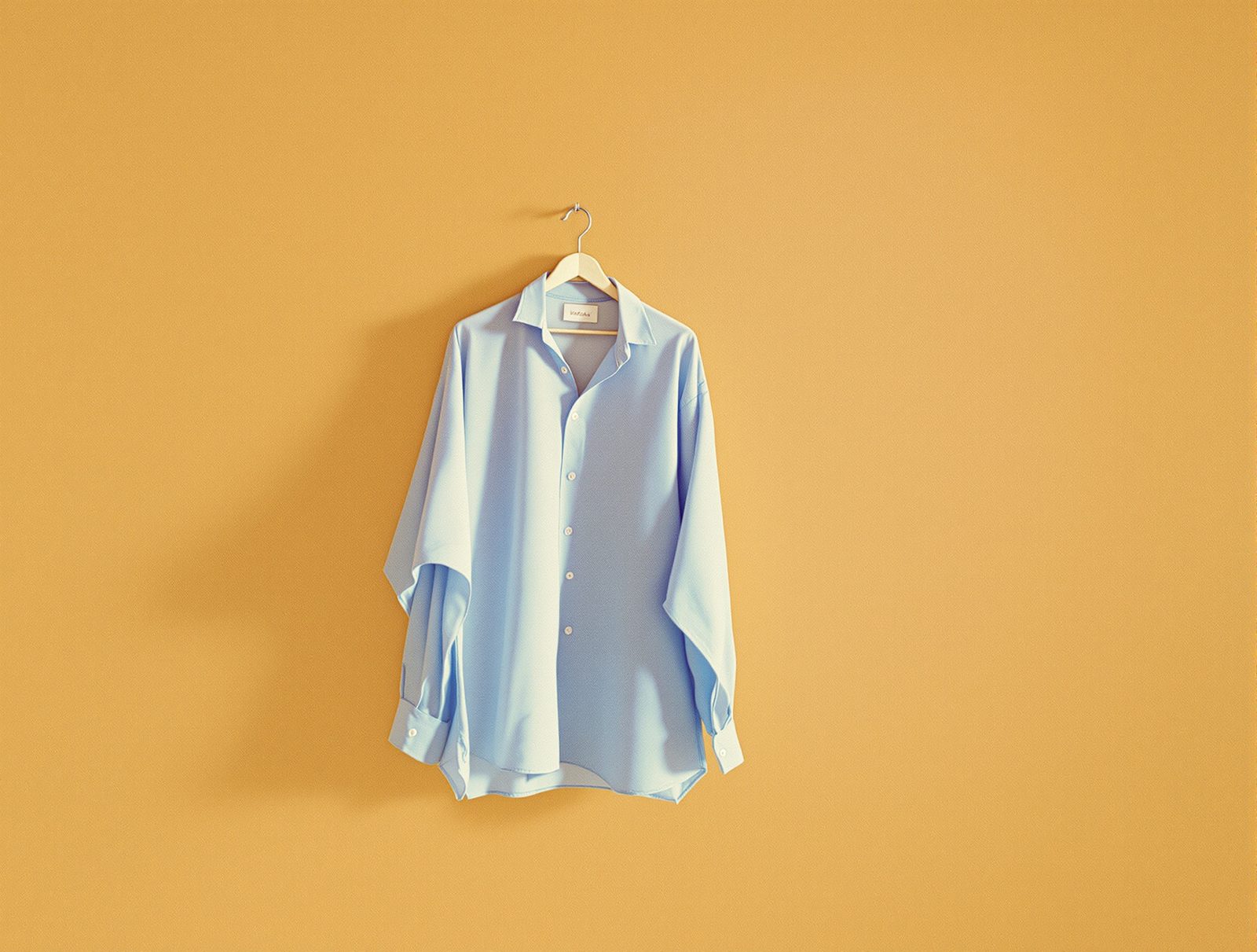 Chemise bleue suspendue sur un cintre en bois epais sur fond neutre chaud pour un sechage sans plis