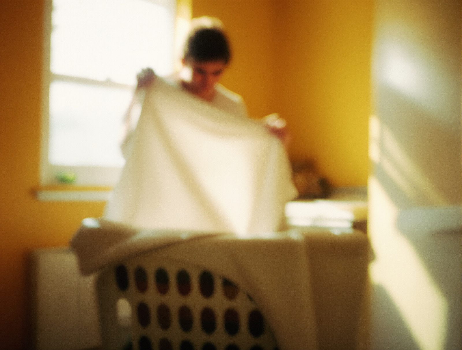 Silhouette de dos secouant une chemise blanche avant de la suspendre pour eviter les faux plis au sechage