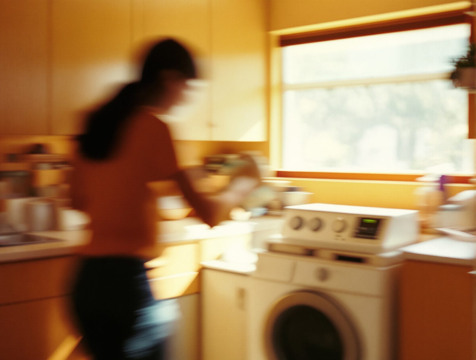 personne de dos versant un produit anti-calcaire dans le tambour du lave-linge en laverie